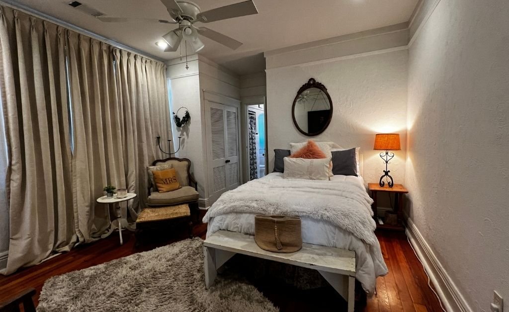 Bedroom inside the Clancy House featuring a neatly made bed, vintage furnishings, soft lighting, and original wood floors in a restored historic room.