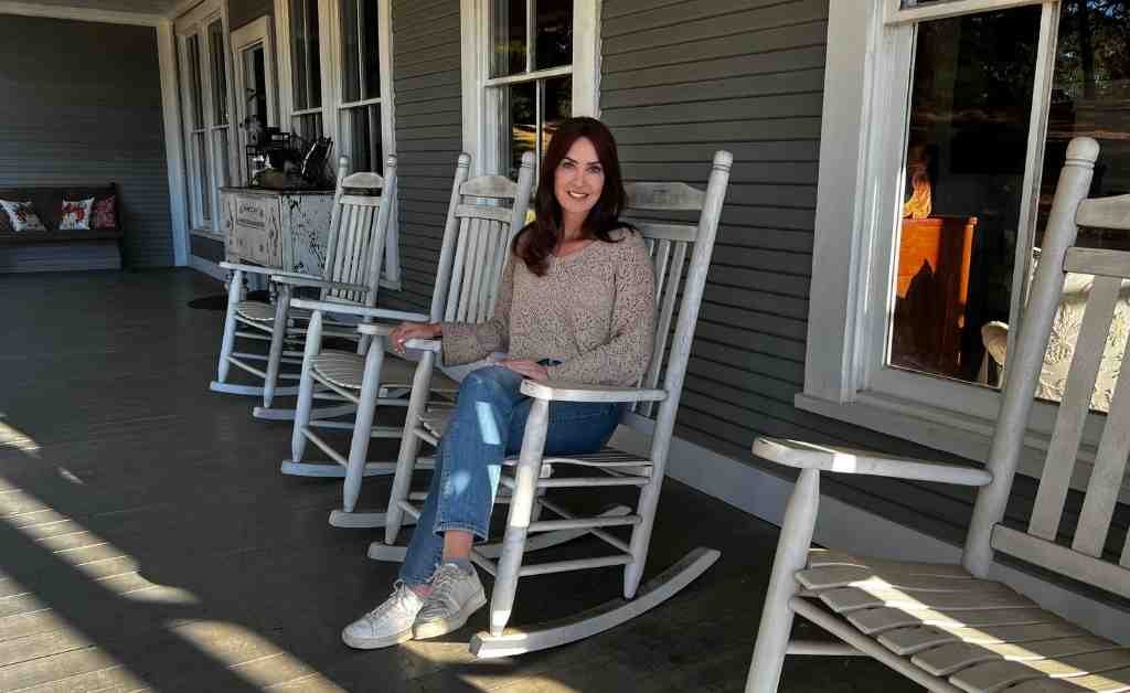 Karen LeBlanc sitting in a white rocking chair on the front porch of the Dover House in Florien, Louisiana