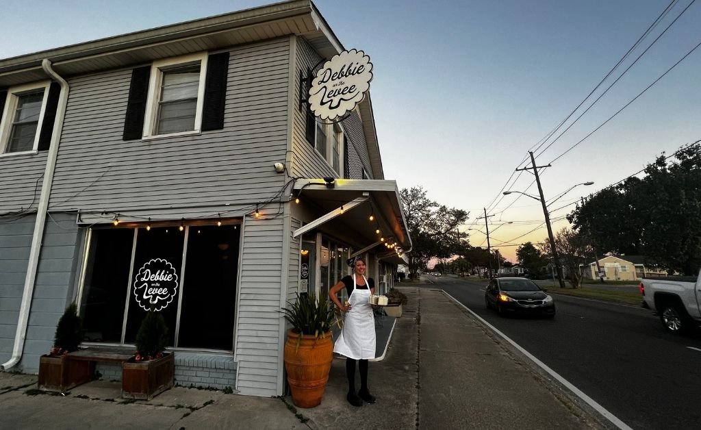 Exterior of Debbie on the Levee café in Kenner, Louisiana, with staff member standing outside at sunset holding desserts.