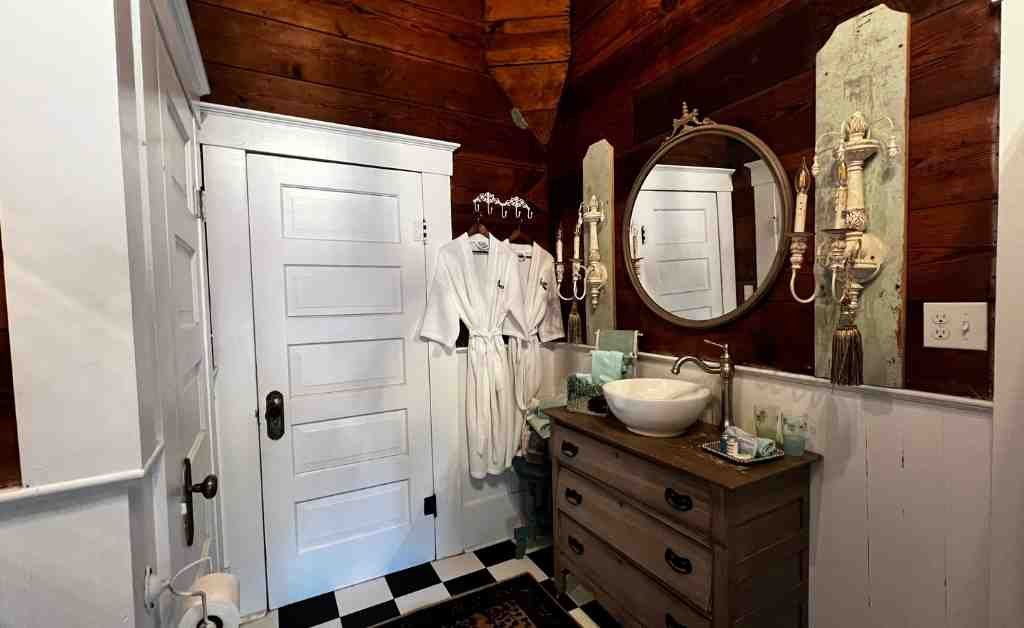 Bathroom at the Dover House in Florien with a vintage vanity, vessel sink, wall sconces, and black-and-white tile floor