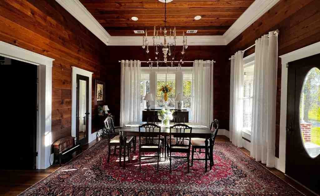 Dining room at the Dover House in Florien with a long table, chandelier, wood-paneled walls, and tall windows