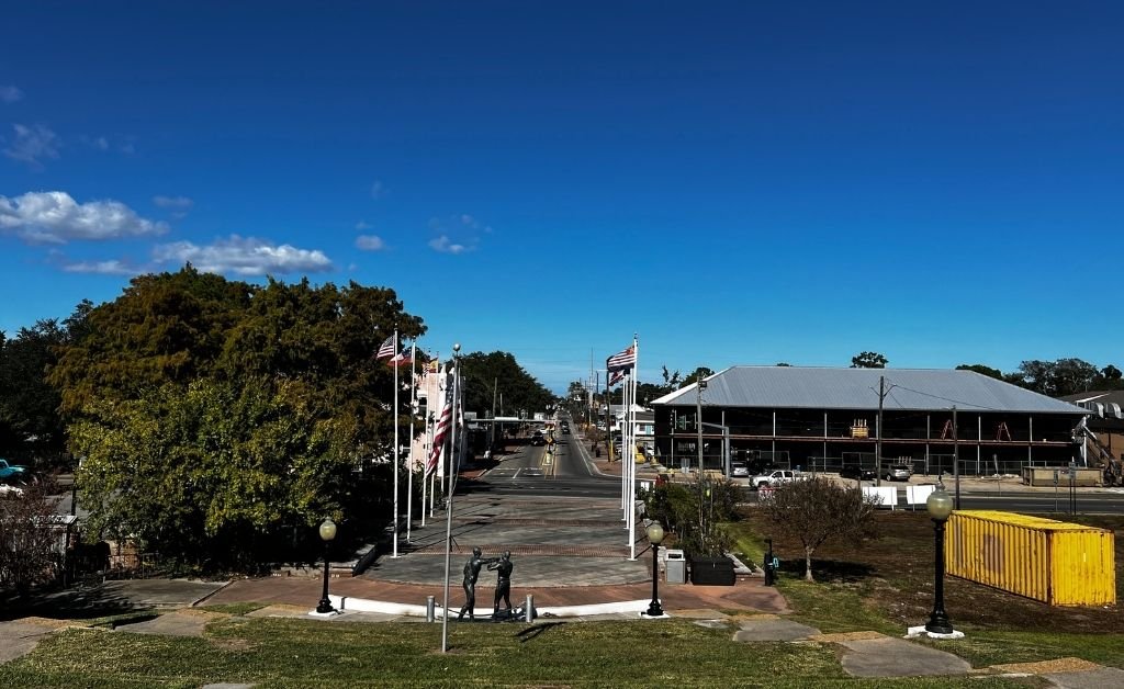 Elevated view of a small-town street lined with American flags, brick walkways, and buildings under a clear blue sky.