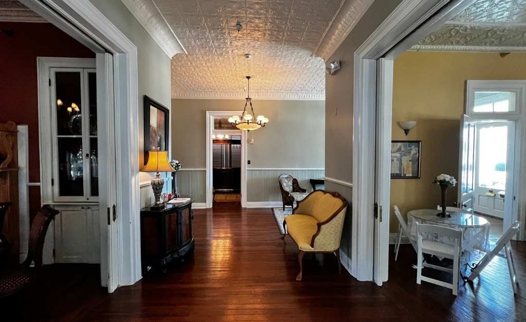 Interior view of The Caldwell House Bed and Breakfast in Abbeville, Louisiana, showing connected sitting rooms, pressed tin ceilings, and original hardwood floors.