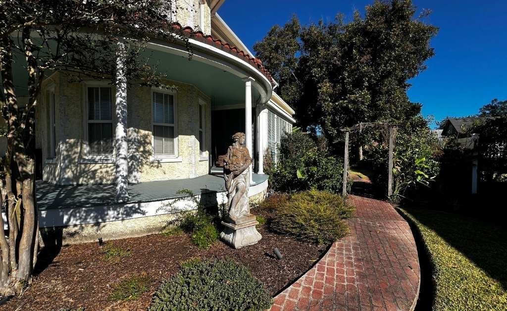 Side view of The Caldwell House Bed and Breakfast in Abbeville, Louisiana, showing the wrap around porch, brick walkway, garden path, and exterior details.