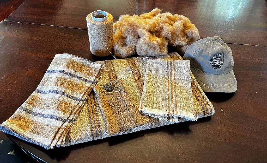 Handwoven brown cotton textiles, raw cotton, yarn, and an Acadiana brown cotton cap displayed at Cajun Prairie Farm in Arnaudville, Louisiana.