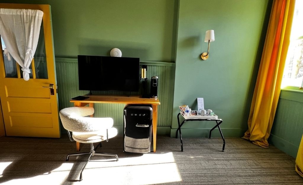 Seating area in the Accessible Poolside King room at Hotel Klaus with writing desk, television, green walls, yellow door, and sunlight from the courtyard.