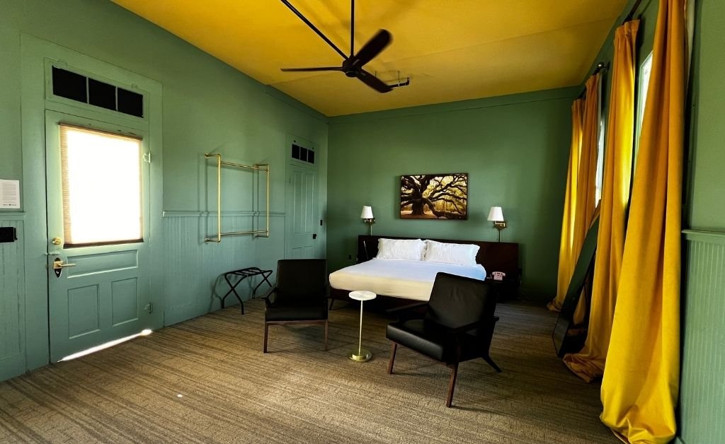Accessible Poolside King room at Hotel Klaus with king bed, seating area, green walls, and yellow curtains opening toward the courtyard.