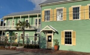 Exterior of Hotel Klaus in Washington, Louisiana, showing the restored historic green building with yellow shutters, front entrance, and upper balcony overlooking the street.