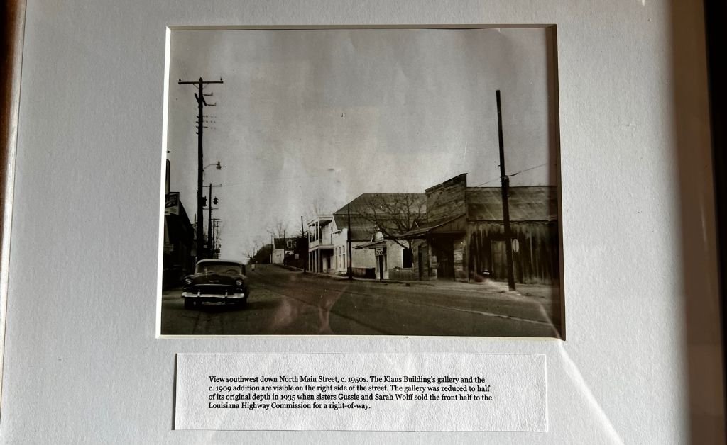 Historic black-and-white photograph of North Main Street in Washington, Louisiana, in the 1950s, showing the Klaus Building with its gallery and surrounding storefronts.