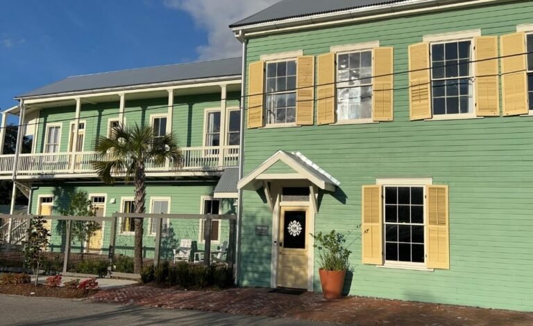 Exterior of Hotel Klaus in Washington, Louisiana, showing the restored historic green building with yellow shutters, front entrance, and upper balcony overlooking the street.