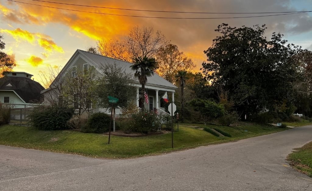 Historic home on a quiet corner in Washington, Louisiana, framed by trees and a colorful sunset sky.