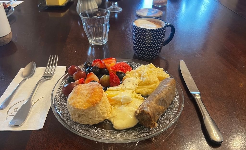 Breakfast plate at Maison Stephanie with eggs, boudin, a homemade biscuit, fresh fruit, and coffee on a wooden table.