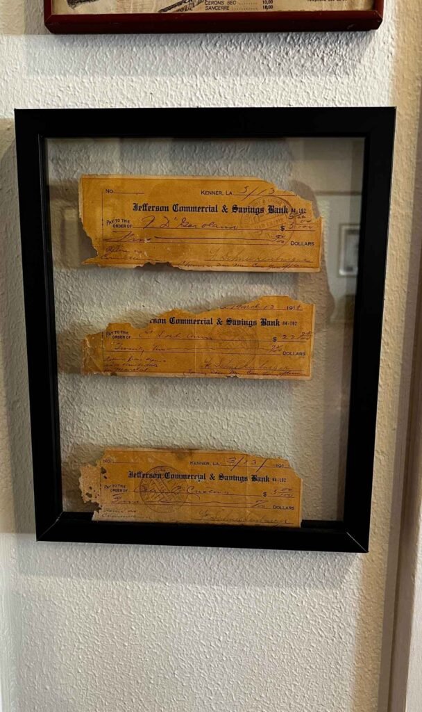 Framed historic checks from Jefferson Commercial & Savings Bank displayed inside the Clancy House, showing handwritten dates and amounts from the early 1900s in Kenner, Louisiana.