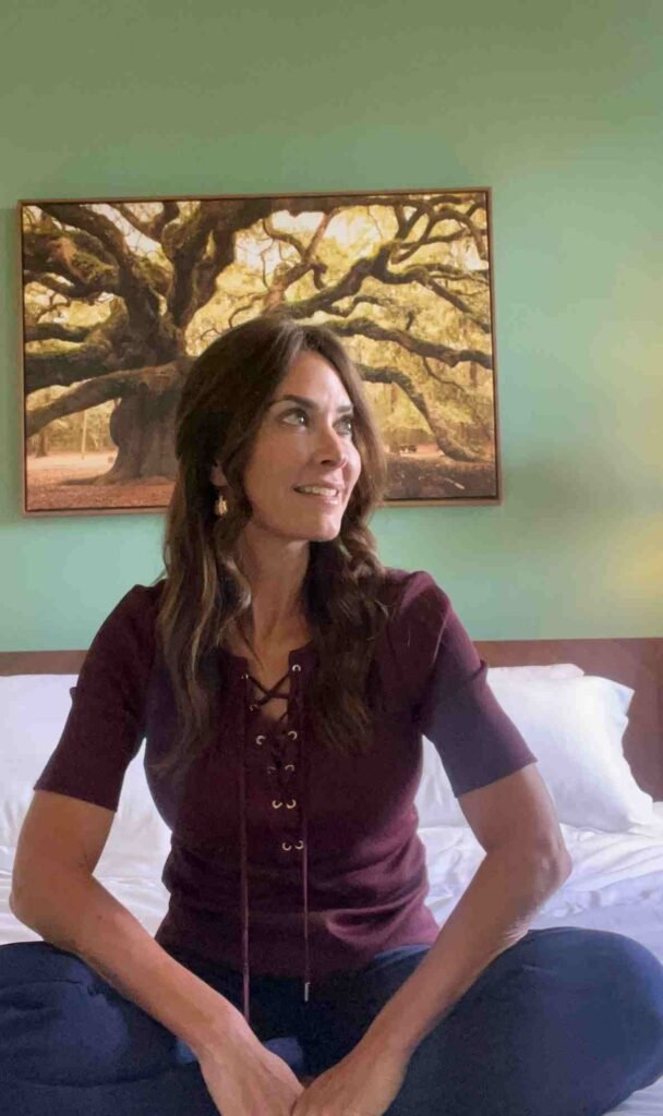Karen LeBlanc sitting on the bed inside a Hotel Klaus guest room, with green walls and framed artwork behind her.