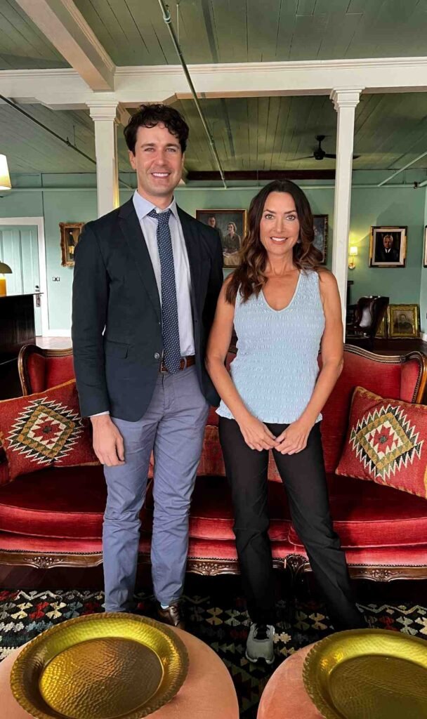Karen LeBlanc and Stephen Ortega standing together in the Portrait Lounge at Hotel Klaus, with vintage seating, framed portraits, and soft green walls in the background.