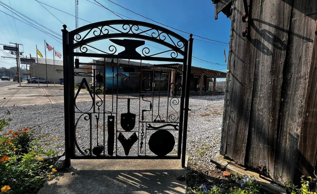 Hand-forged iron gate with blacksmith tools and anvil design at the Sam Guarino Blacksmith Shop Museum in Abbeville, Louisiana.