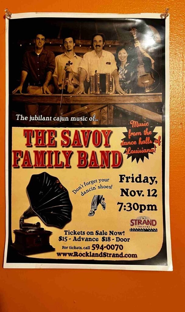 A vintage-style concert poster shows a sepia photograph of five musicians from The Savoy Family Band posing with a violin, accordion, and guitar above a yellow advertisement for their Cajun music show. The event is scheduled for Friday, Nov. 12 at 7:30 pm at the Strand Theatre in Rockland, Maine, with ticket prices of $15 in advance or $18 at the door. The poster urges attendees to “Don’t forget your dancin’ shoes!”
