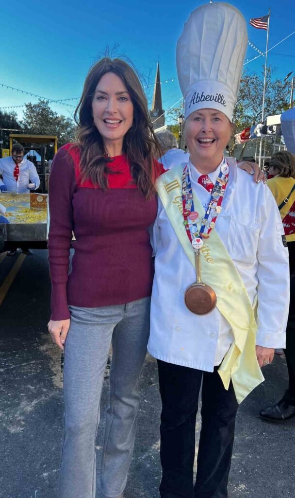 Karen LeBlanc stands with a Chevalier of the Giant Omelette Celebration, wearing ceremonial chef attire and medal, at the skillet in downtown Abbeville.