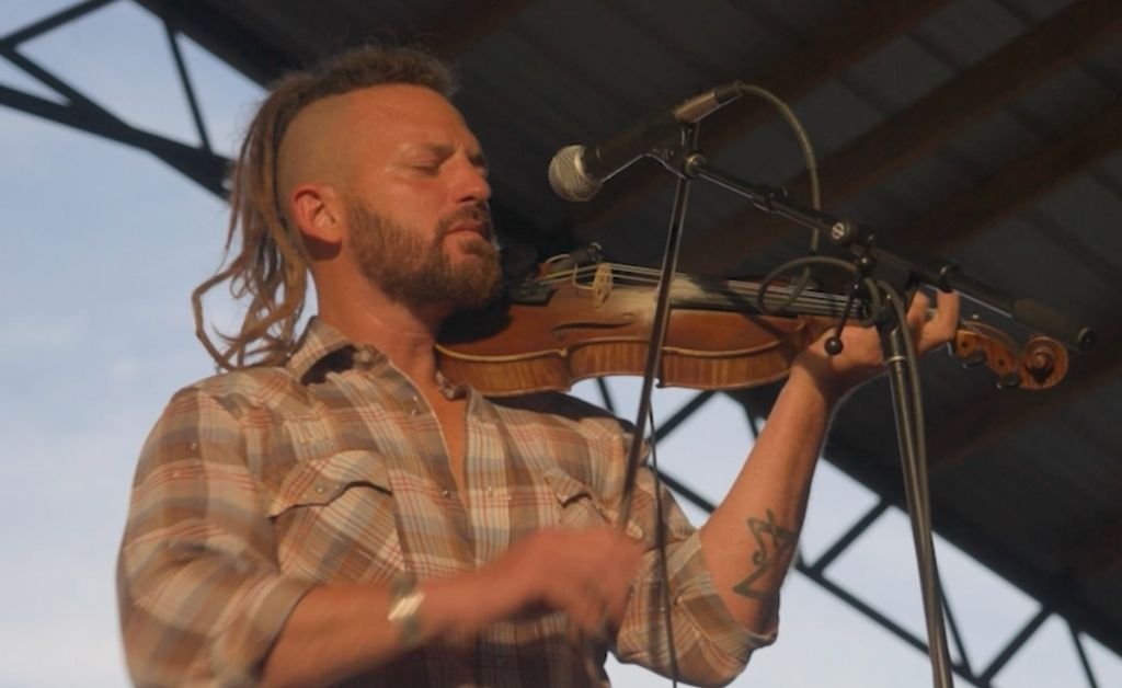 Close-up of Jourdan Thibodeaux playing the fiddle with his eyes closed during a performance.