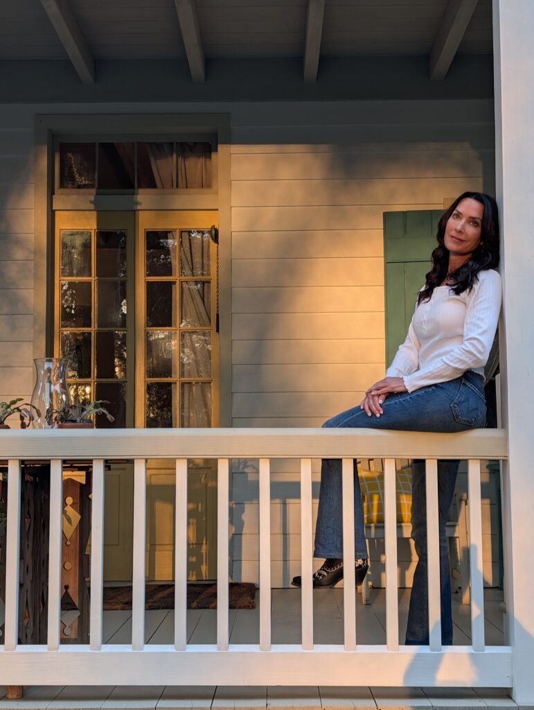 Karen sitting on the white railing of a porch at Maison Madeleine during the golden hour.
