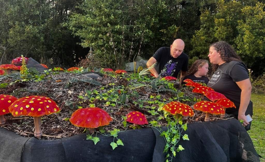 Dr. Brandon Ballengée, Aurore Ballengée, and their daughter Lily inspect a "bio-artwork" mound featuring several red-and-yellow sculptural mushrooms at Atelier de la Nature.