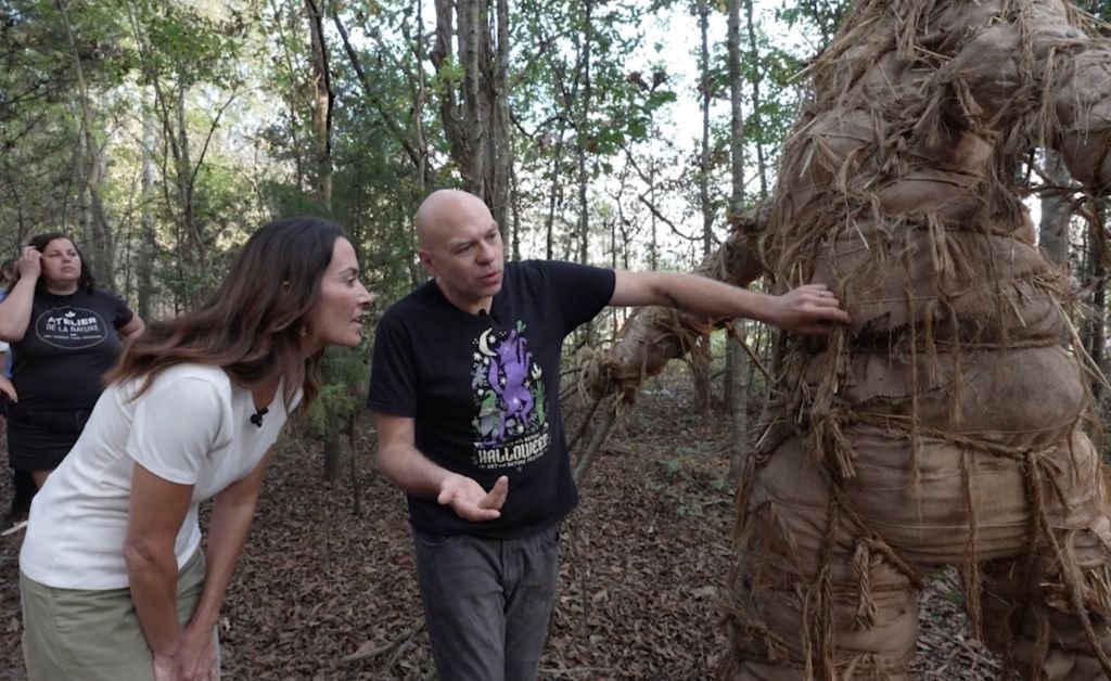 Dr. Brandon Ballengée explains the construction of a large, straw-wrapped sculptural form to Karen LeBlanc on a wooded trail at Atelier de la Nature.