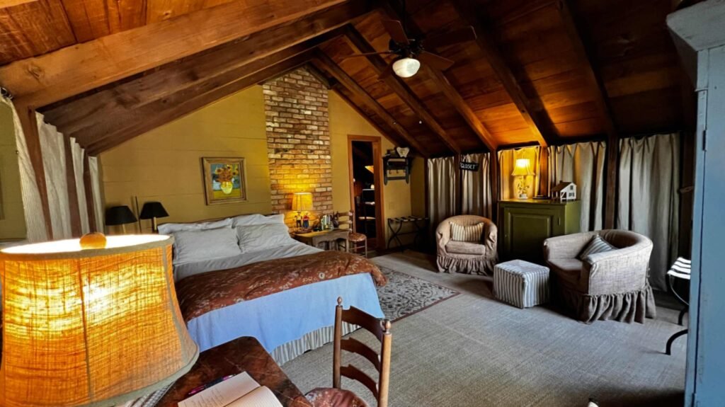 A spacious guest room with yellow walls, a brick chimney, a large bed, and comfortable armchairs.