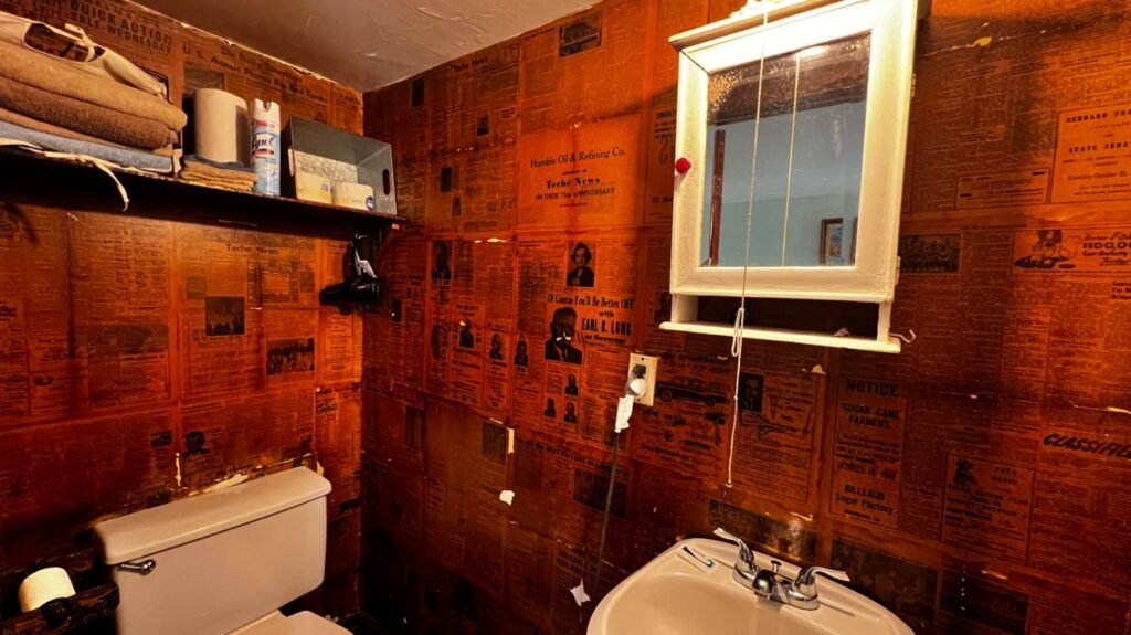 A small bathroom in Bocephus' Cajun Cabin at Bayou Cabins in Breaux Bridge, Louisiana, where the walls are uniquely covered in vintage 1949 newspapers as wallpaper.