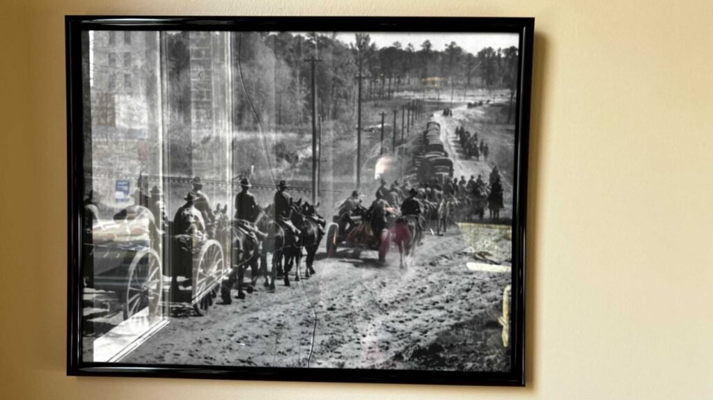 A framed black-and-white historical photograph on display at the Hotel Bentley showing a military convoy of horse-drawn artillery and soldiers on horseback during the 1940s Louisiana Maneuvers in Central Louisiana.