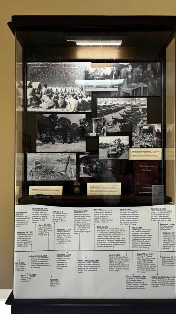 A vertical museum display at the Hotel Bentley in Alexandria, Louisiana, featuring historical black-and-white photos of military camps and soldiers, paired with a detailed chronological timeline of the Louisiana Maneuvers and World War II.
