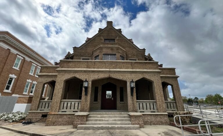 The image captures the imposing sand-blasted concrete facade of the 1914 DeRidder Gothic Jail. The structure’s 'Collegiate Gothic' design features elegant pointed arches and a majestic staircase, famously known as the site of a grim 1928 double execution that fueled its reputation as one of Louisiana’s most haunted locations.