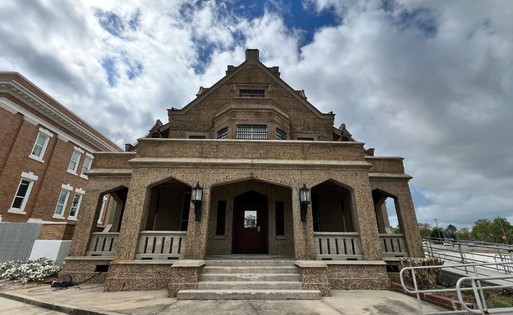 The image captures the imposing sand-blasted concrete facade of the 1914 DeRidder Gothic Jail. The structure’s 'Collegiate Gothic' design features elegant pointed arches and a majestic staircase, famously known as the site of a grim 1928 double execution that fueled its reputation as one of Louisiana’s most haunted locations.