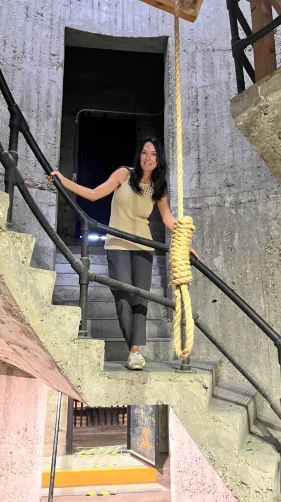 A woman stands on the concrete spiral staircase of the DeRidder Gothic Jail, posing next to a replica noose that hangs in the center of the stairwell.