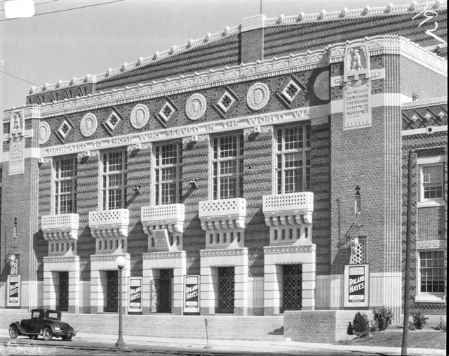 A black-and-white historical photograph from circa 1929 showing the highly ornamented brick and limestone front facade of the Shreveport Municipal Memorial Auditorium. The building features colossally-scaled pilasters, intricate brickwork balconies, and decorative bas-relief panels. Posters on the ground level advertise a concert by Roland Hayes, a pioneering African American tenor. A vintage car is parked on the street in the lower-left foreground.